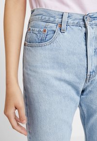 Ljusblå denimjeans med hög midja, fem fickor och koppardetaljer. Tyget har en något sliten textur med kontrasterande sömmar.