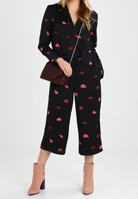 Sort jumpsuit med pink og røde læbestiftskilte, med et skræddersyet design, lange ærmer og brede, korte ben. Kompletteret med en bordeaux håndtaske.