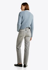 Pull en tricot texturé bleu clair avec un col rond, associé à un jean taille haute gris clair et des chaussures noires.