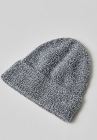 Grijze gebreide beanie gemaakt van pluizig garen, met een gestructureerd oppervlak en glanzende draden, en een klein metalen label op de rand.