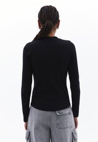 Maglietta nera a maniche lunghe con un design aderente, scollatura rotonda e un orlo leggermente curvo, abbinata a pantaloni cargo grigi chiari con tasche applicate.