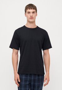 T-shirt noir à manches courtes en coton. Il présente un col rond et une coupe décontractée, sans motifs ni accents visibles.