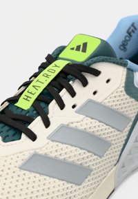 Chaussure de sport légère avec une tige en mesh crème, des accents teal, des lacets noirs et des rayures grises. Étiquette verte marquée "HEAT.RDY" sur la languette.