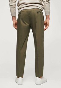 Pantaloni verde oliva dal taglio slim, dotati di due tasche posteriori con bottoni e una trama di tessuto liscia. Abbinati a sneaker bianche.