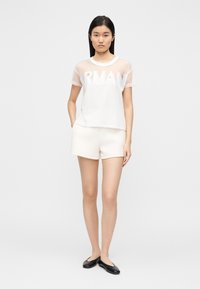 Λευκό μπλουζάκι από δίχτυ με τη λέξη "ARMANI" τυπωμένη σε μεγάλα γράμματα. Συνδυασμένο με κρεμ σορτς και μαύρα επίπεδα παπούτσια. Με λεία υφή, άνετη εφαρμογή.