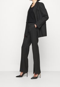 Schwarzes, doppelt geknöpftes Blazer über einem schwarzen Tanktop, kombiniert mit schwarzen weit geschnittenen Hosen und spitzen High Heels. Einfaches und elegantes Design.