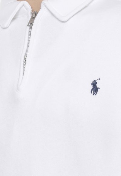 Camicia bianca con colletto e cerniera, con un piccolo logo ricamato scuro di un giocatore di polo sul lato sinistro del petto.