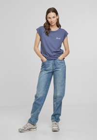 Marineblaue Kurzarm-T-Shirt mit einem gestickten weißen Logo, kombiniert mit hellblauen, locker sitzenden Jeans und neutral gefärbten Sneakers.