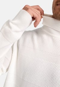Hvit strikket turtleneck genser med teksturerte horisontale striper og ribbestrikkede mansjetter. Stoffet har et mykt, svakt hevet mønster.