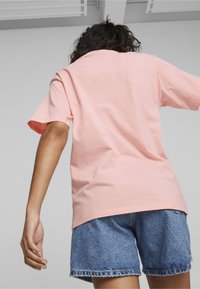 Camiseta de algodón de color rosa claro con mangas cortas, corte amplio y dobladillo curvado, combinada con pantalones cortos de mezclilla azules con bordes deshilachados.