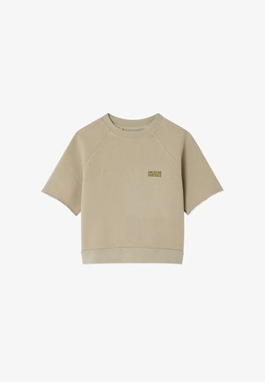 Garçon souriant portant un sweat-shirt beige "American Vintage" superposé à une chemise verte, avec une écharpe bleu clair nouée autour du cou.
