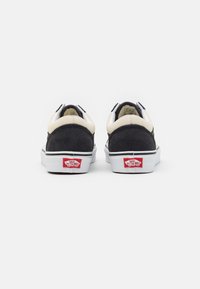 Schwarze Wildleder- und cremefarbene Leder-Sneaker mit weißen Sohlen, versehen mit einem roten Vans Off The Wall-Logo an der Ferse. Minimalistisches Design mit klassischer Form.