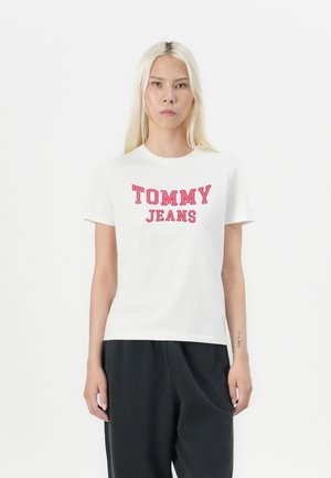 T-shirt blanc à manches courtes arborant le texte rouge "TOMMY JEANS". Fabriqué en coton, avec une coupe classique et un col rond. Associé à un pantalon sombre.