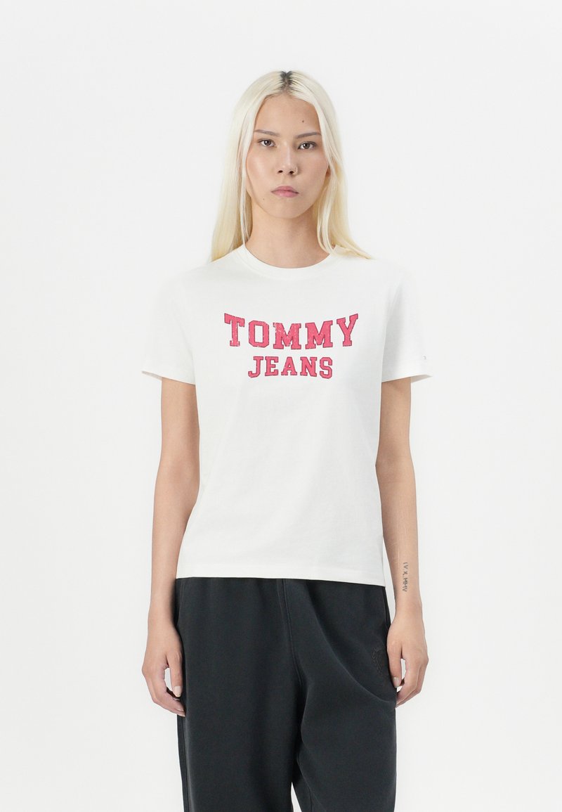 Camiseta de manga corta blanca con texto rojo "TOMMY JEANS". Hecha de algodón, con un corte clásico y escote redondo. Combinada con pantalones oscuros.