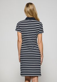 Abito polo a righe blu navy e bianche con colletto a risvolto, maniche corte e taglio dritto che arriva a metà coscia. Tessuto dalla superficie liscia.