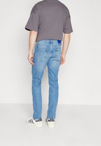 Jeans i ljusblå denim med smal passform, utrustade med bakfickor och en märkesetikett. Matchas med en grå, kortärmad T-shirt och sneakers.