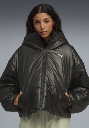 Zwarte pufferjack met een glanzende afwerking, oversized capuchon en ritssluiting. Voorzien van een klein wit logo op de linkerkant van de borst en elastische manchetten.
