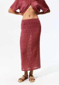 Gehaakte rok in een gestructureerde, stoffige rozenkleur met een aangesloten taille en een lange lengte, gecombineerd met eenvoudige sandaaltjes met bandjes.