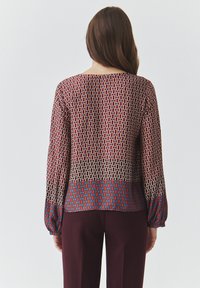 Langsleeve top in rode en blauwe geometrische patronen, met een ronde halslijn en elastische manchetten, gecombineerd met donkere broeken.