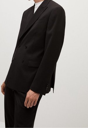 Mężczyzna w czarnej, dwurzędowej marynarce z klapami typu notch i przednimi kieszeniami z patkami, noszący białą koszulę.