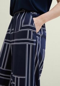Navy blue wide-leg pants with a white geometric pattern, featuring an elastic waistband and side pockets, made of smooth fabric.