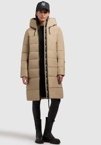 Beige Pufferjacke mit knielangem Design, Seitentaschen und einem Frontreißverschluss mit Logoband. An einem Kordelzug befestete Kapuze.