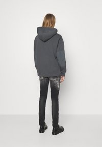 Felpa con cappuccio grigia scura con un design bicolore, caratterizzata da una vestibilità comoda. Indossata con jeans neri strappati e scarpe nere.