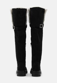 Czarne zamszowe kozaki za kolano z miękką, sztuczną futrzaną wyściółką i srebrnymi klamrami. Wyposażone w zamki błyskawiczne dla łatwego zakładania oraz masywną czarną podeszwę.