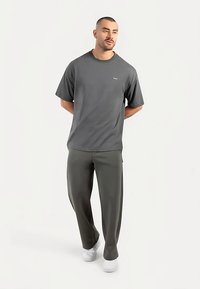 Gray short-sleeve t-shirt, round neckline, paired with dark green tapered pants, both in a smooth fabric. Model wearing white sneakers.