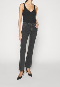 Top de tirantes negro acanalado combinado con unos vaqueros negros de tiro alto y de pernera acampanada con un dobladillo sin terminar. El look se completa con unos zapatos de tacón negro de punta. 
