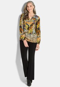Langärmlige Bluse mit tropischem Blumen- und Leopardenmuster in Gelb, Grün und Braun, kombiniert mit schwarzen geraden Hosen und Stiefeletten.