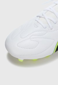 Biały syntetyczny but piłkarski o teksturowanej powierzchni, subtelnym przeszyciu i zielonej podeszwie. Posiada sznurowany design i gładki czubek.