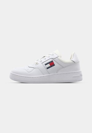 White sneaker made of smooth leather with round toe, flat laces, and rubber sole. Features a blue, red, and white logo patch on the side.
