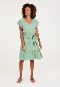 Grünes, V-Ausschnitt-Kleid mit kurzen Ärmeln, Bindeband in der Taille und gestuftem Saum. Hergestellt aus strukturiertem Stoff, mit einem lässigen, fließenden Design.