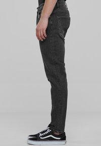 Fekete skinny farmernadrág, öt zsebbel, cipzáras résszel és övhurkokkal, fekete-fehér sneaker cipőkkel párosítva.
