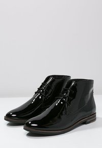 Botas de tobillo de charol negro con un diseño elegante, punta redonda, cordones en la parte delantera y pequeño tacón apilado. Textura suave con costuras sutiles.