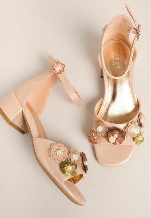 Õrnalt roosas toonis kõrged sandaalid laia rihmaga, lillemotiividega kaunistatud ja väike kand; siledapinnaline metallilise sisevoodriga.