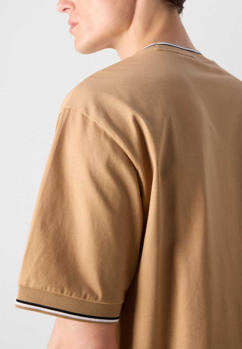 Hombre con una camisa de manga corta color beige y puños acanalados, con rayas en blanco y negro, visto desde atrás y de lado.