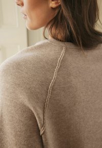 Beige gebreide trui met een textuurnaad langs de schouder, gemaakt van een zachte, comfortabele stof en heeft een relaxed fit.