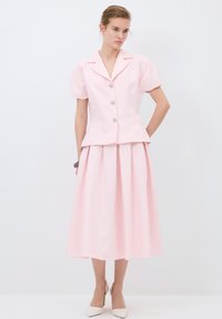 Completo rosa chiaro composto da un blazer aderente a maniche corte con vita a peplo e quattro bottoni decorativi, abbinato a una gonna midi plissettata.