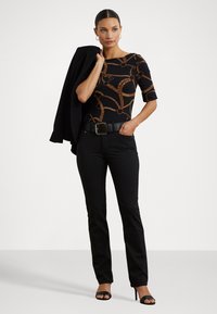 Sorte, tettsittende bukser kombinert med en mønstret topp med brune kjededesign. Overtøyet inkluderer en svart jakke og et svart belte med en sølvspenne.