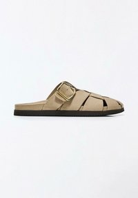 Bézs színű szarvasbőr papucs fonott felsőrésszel, nagy arany csattal és lapos fekete talppal.