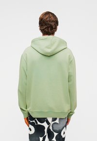 Φούτερ με κουκούλα σε μέντα πράσινο χρώμα με άνετη εφαρμογή, διαθέτει κουκούλα με κορδόνι και ριμπ μανσέτες, συνδυασμένο με ασπρόμαυρο παντελόνι με σχέδια.