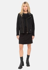 Giacca nera in tela con zip dorate, abbinata a un top nero e una gonna nera fino al ginocchio. Stivali neri trasparenti con tacco. Design semplice e moderno.