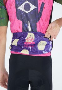Kleurrijke fietsshirt heeft een roze en paarse patroonontwerp met grafische elementen, gecombineerd met zwarte fietsshorts.