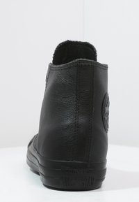 Svart läder höganpassad sneaker med en strukturerad yta, rund logotyp på sidan och en gummisula med "All Star"-märkning.