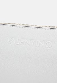 Bílá kožená psaníčko s embosovaným logem "VALENTINO", vybavené zlatým zipem a hladkým texturovaným povrchem. Jednoduchý, minimalistický design.