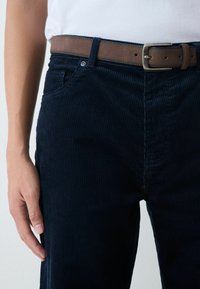 Navy corduroy pants with a textured surface, featuring a brown leather belt and silver buckle. Side pocket detail visible.