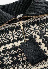Pull zippé noir et blanc avec un motif de flocons de neige, col et poignets côtelés, et un détail de fermeture éclair doré. Texture en tricot douce.