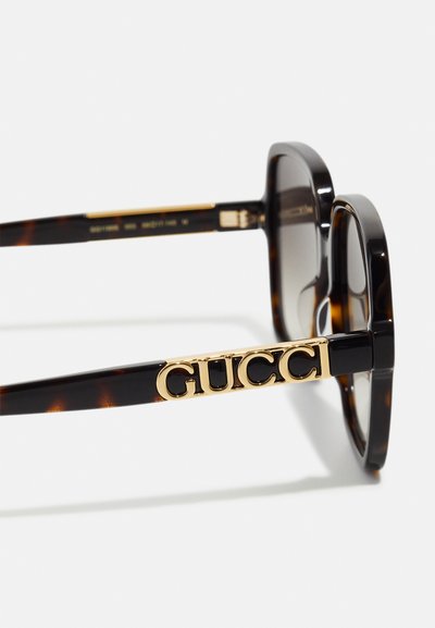 Occhiali da sole tartarugati con montatura spessa, lenti sfumate e logo "GUCCI" in tono oro sulla stanghetta.